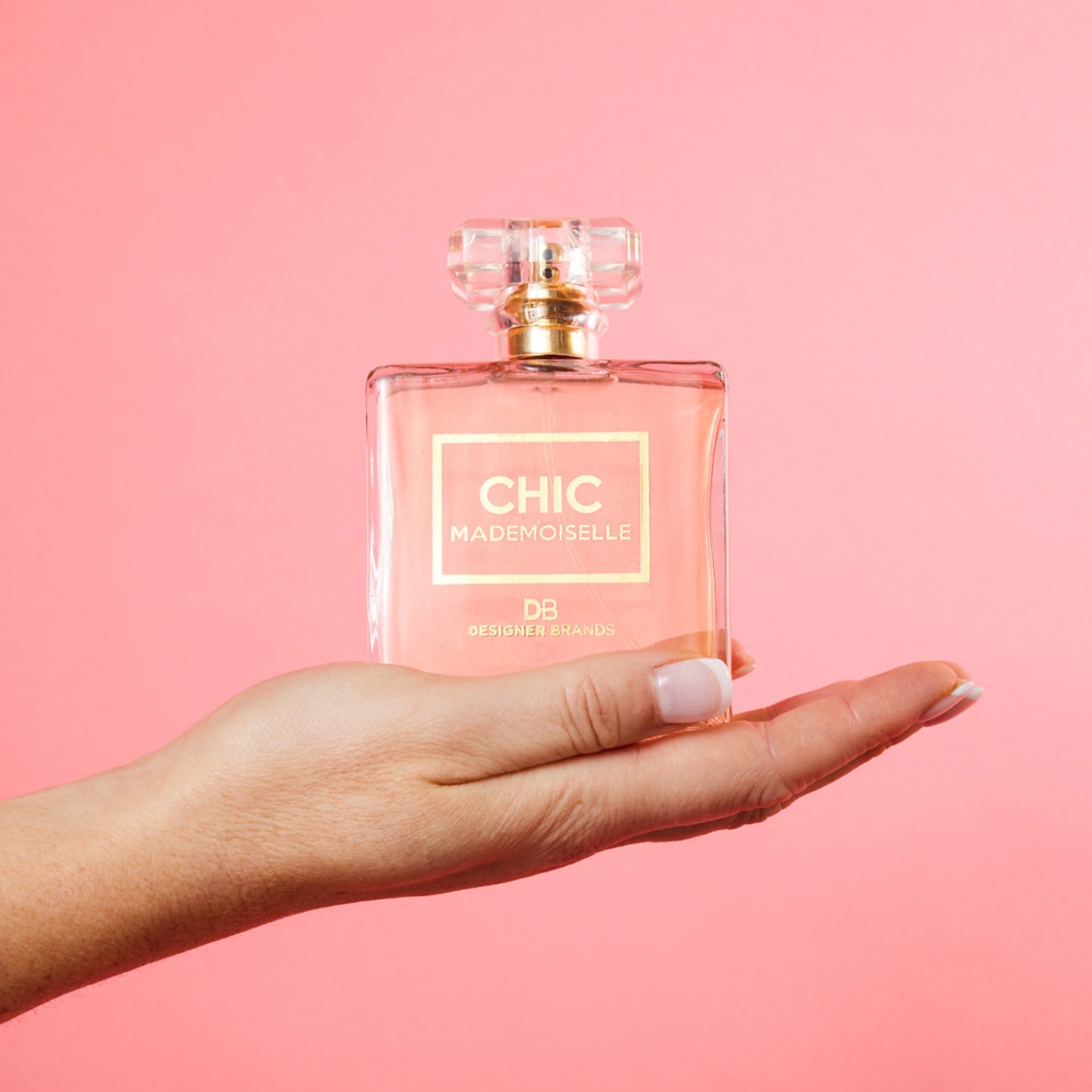 Hand holding a "Chic Mademoiselle" perfume bottle against a pink background. Elegant and stylish fragrance display.
