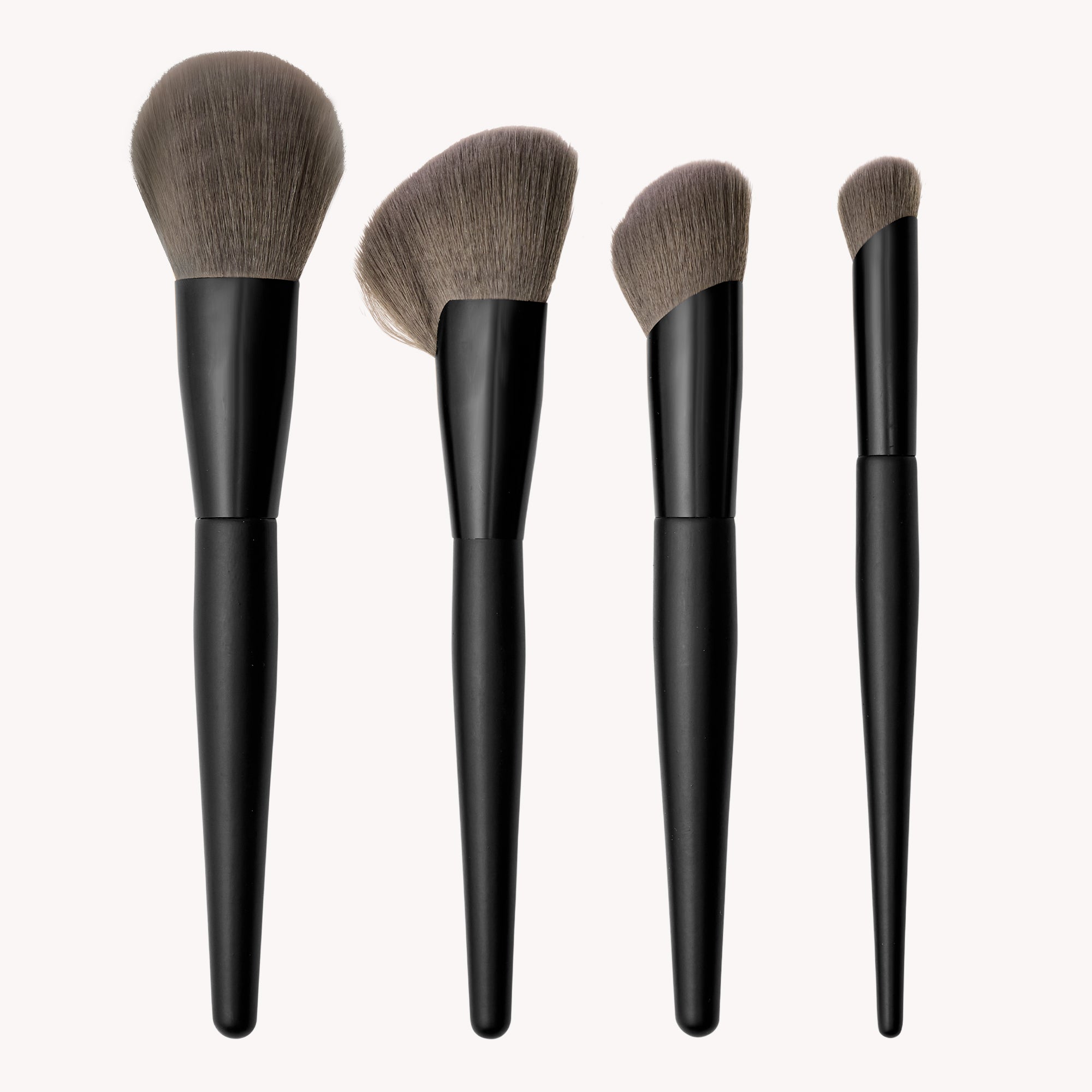 Set of four makeup brushes with black handles on a white background
