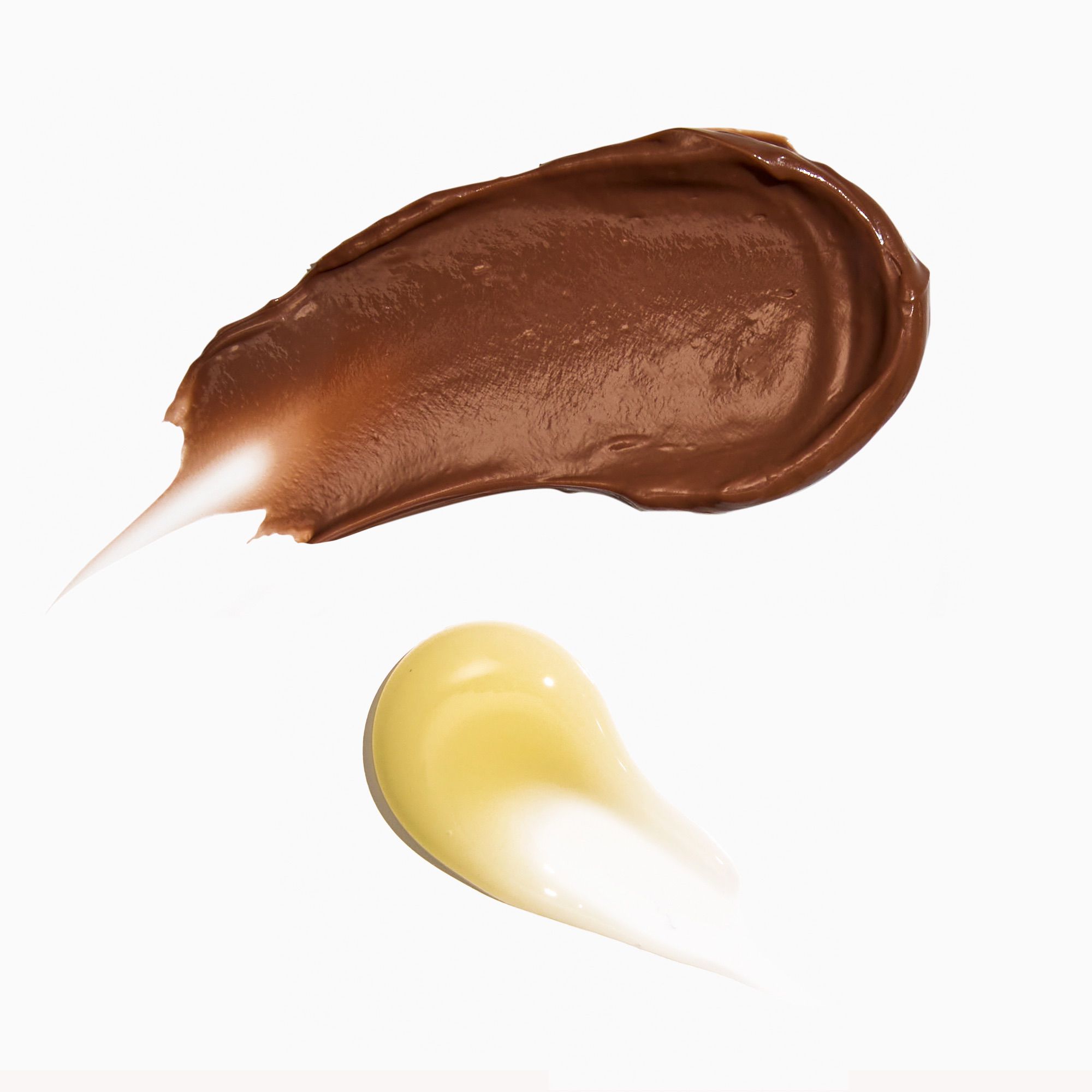 Swatches of brown and yellow makeup cream on a white background