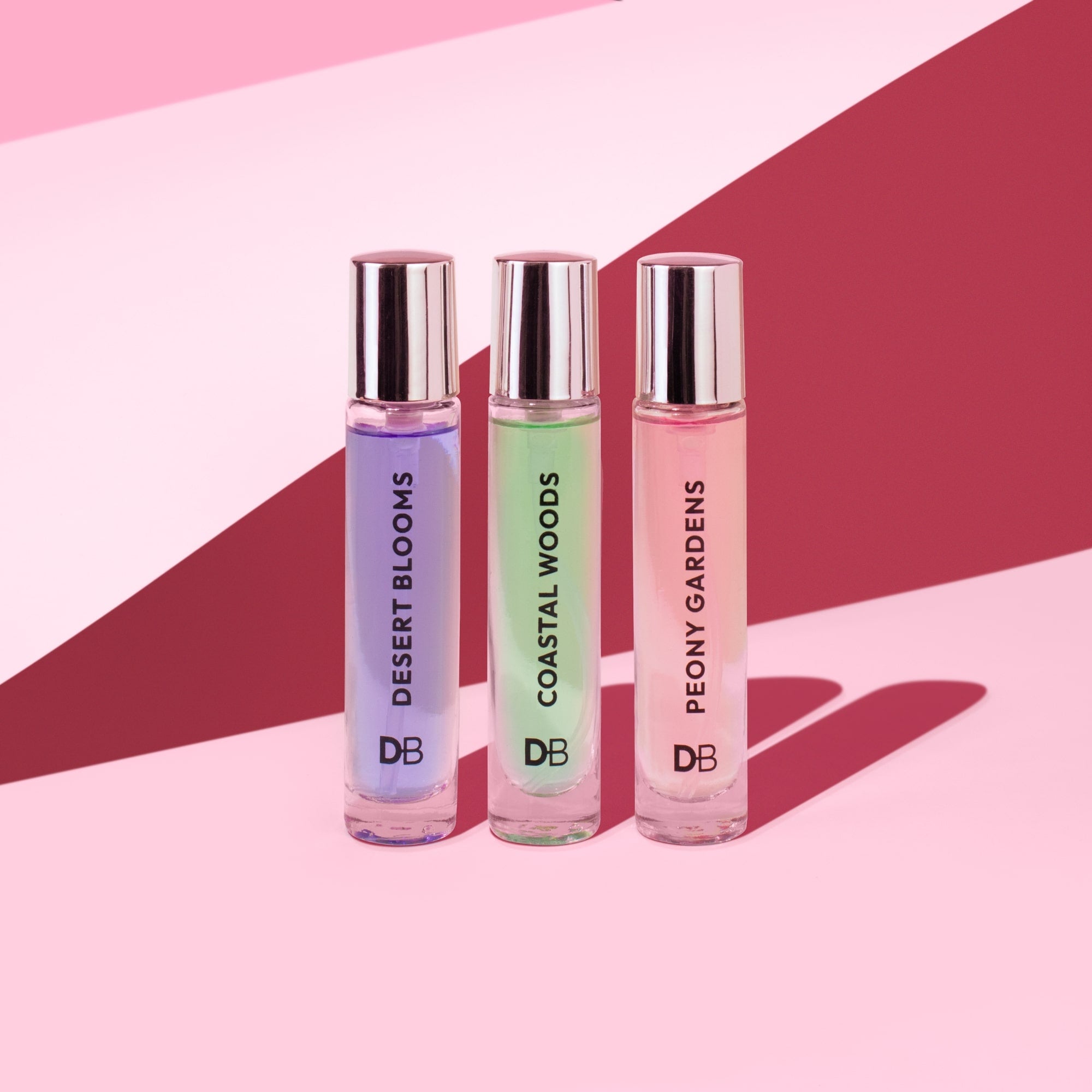 Three perfume bottles labeled 'Desert Blooms', 'Coastal Woods', and 'Peony Gardens' on a pink and red geometric background.