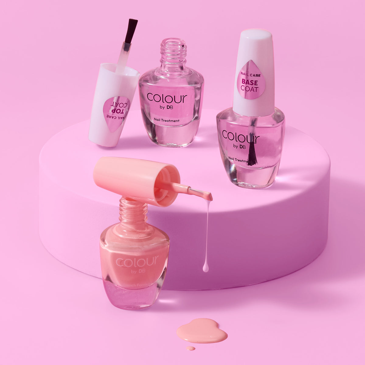 3x nail polish bottles from Colour by DB. Brand from the Nail Care Collection, including a base coat, top coat & nail polish arranged on a pink cylindrical pedestal with a pink background. | colour-kitty-kat