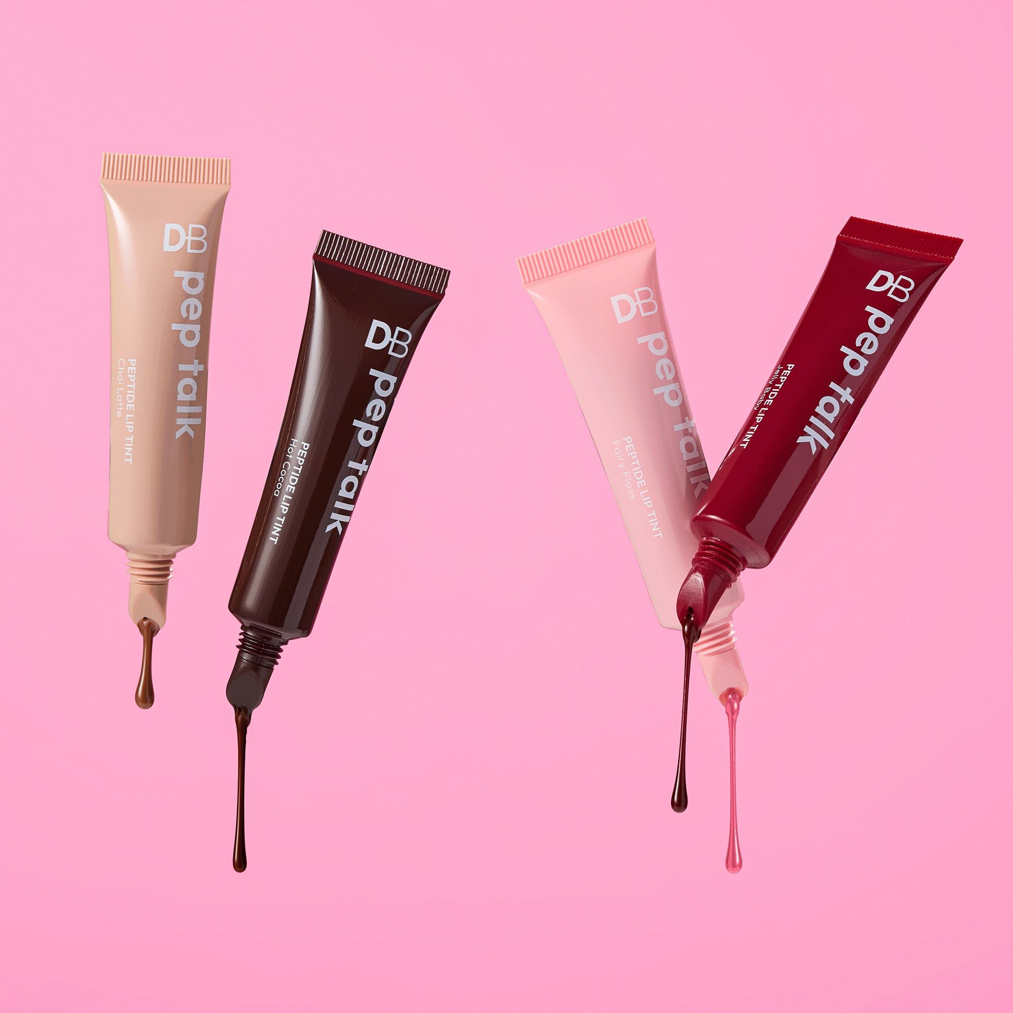 Four DB Pep Talk lip gloss tubes with glossy drips on a pink background, showcasing shades of beige, brown, pink, and red.