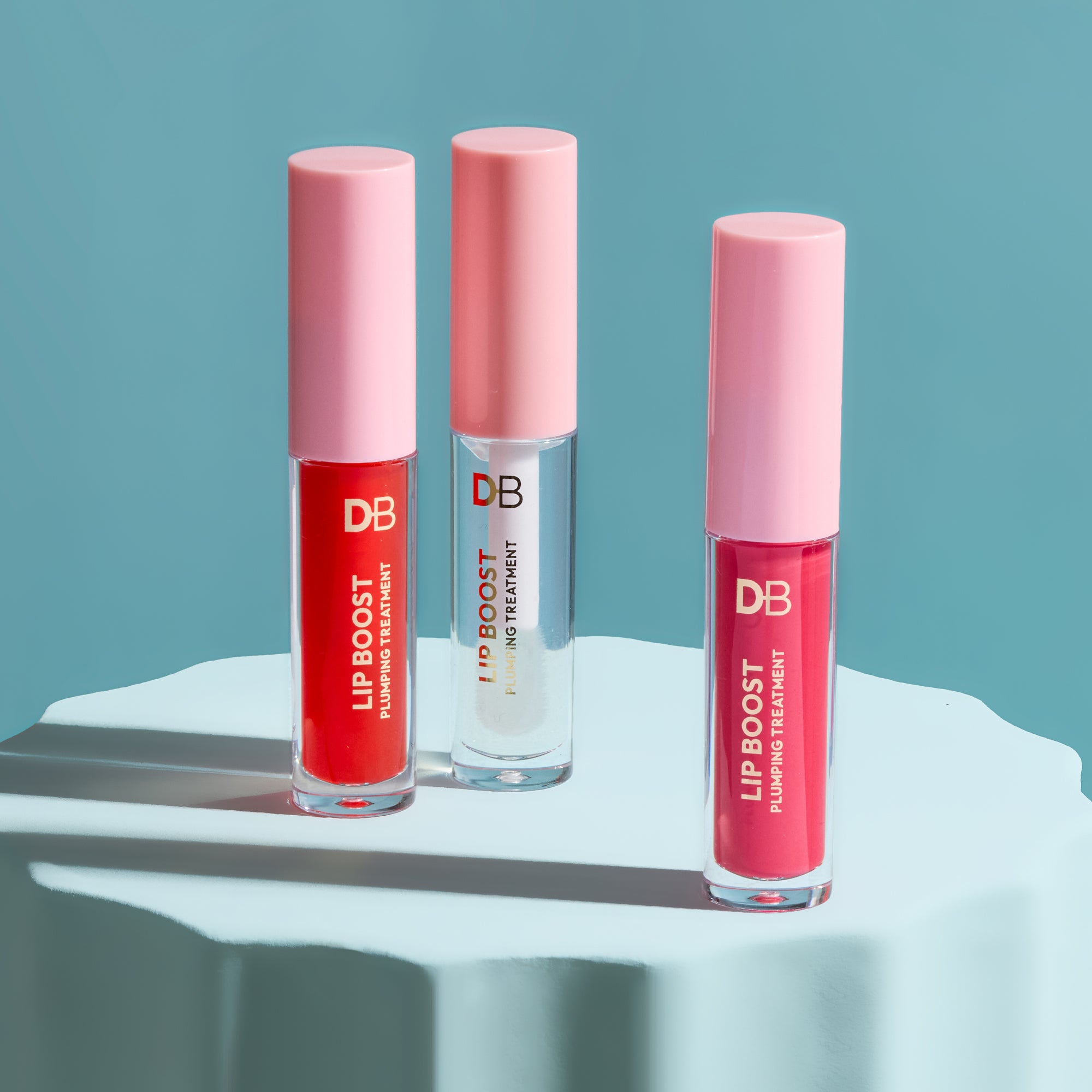 Three lip boost products with pink caps on a white surface against a blue background