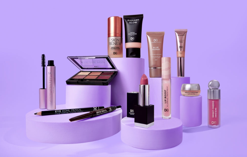 Luxury makeup set on purple stands includes lipstick, eyeshadow palette, mascara, and more. Elegant beauty products against a soft lavender background.