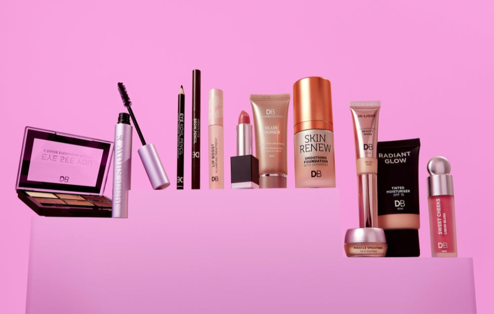 Assorted luxury makeup products displayed against a pink backdrop, featuring lipsticks, mascaras, palettes, and skincare items, exuding elegance.