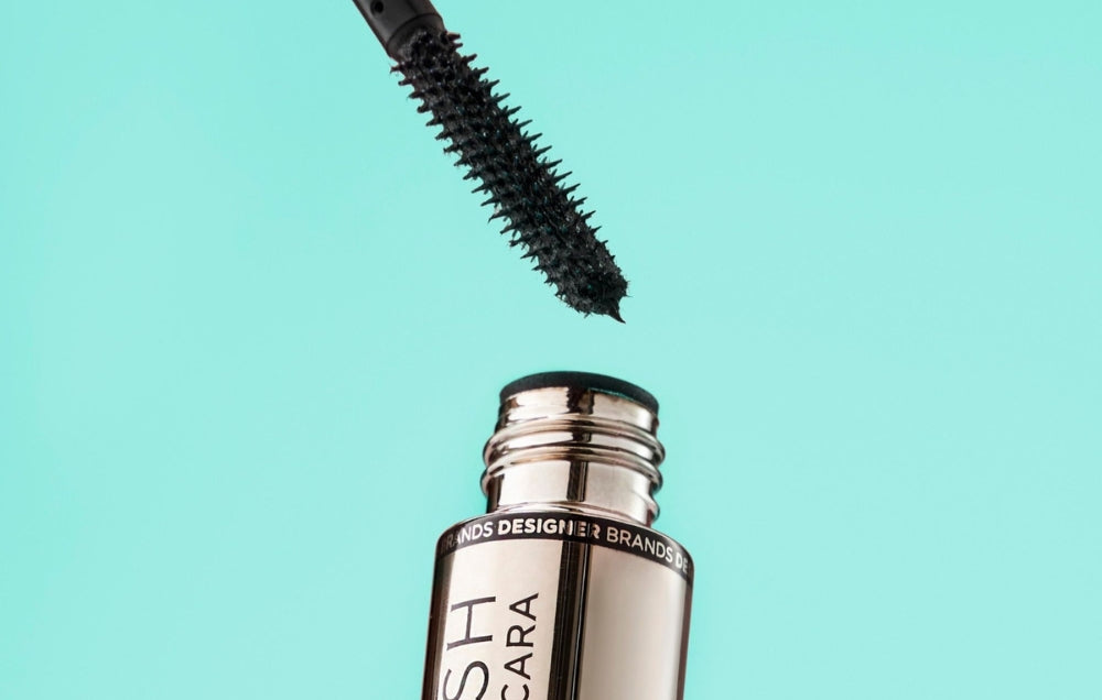 Close-up of a sleek black mascara wand emerging from a glossy silver tube against a turquoise background, exuding luxury makeup elegance.