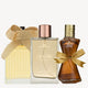 Three elegant perfume bottles: one with a gold ribbon, one with a rose gold cap, and the third with a gold bow and text "DB YOUTH DROP".