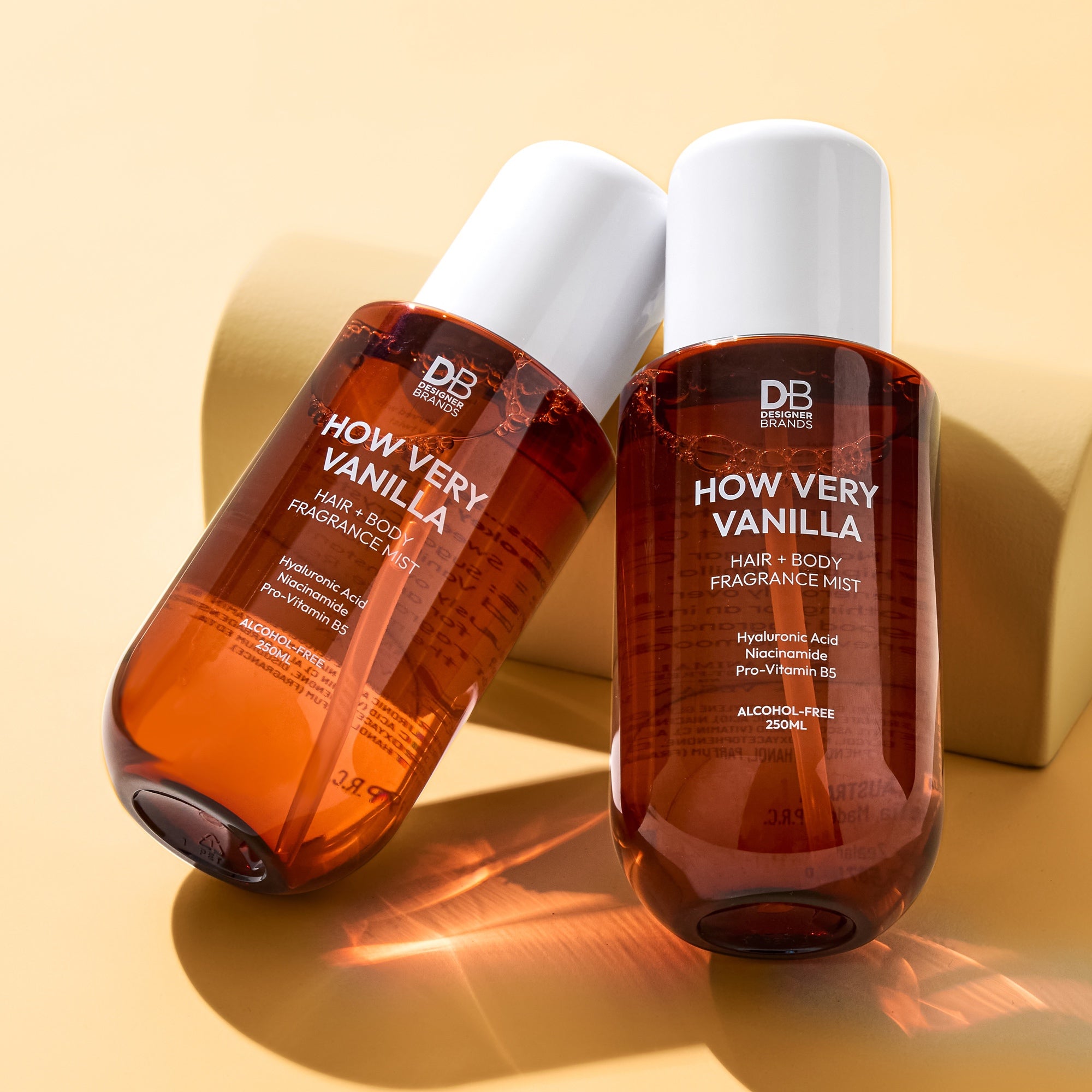 Two bottles of 'How Very Vanilla' hair and body fragrance mist on a beige background