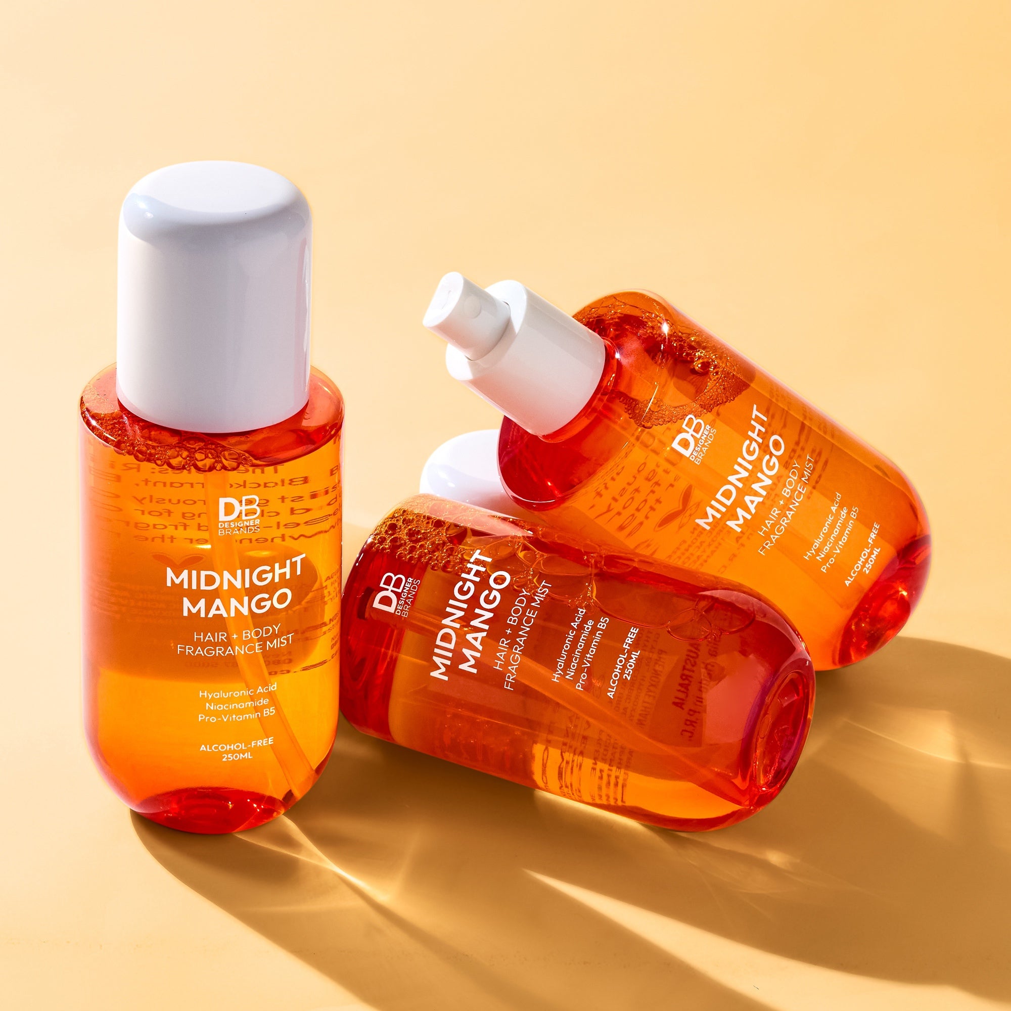 Three bottles of 'Midnight Mango' fragrance mist on a beige background